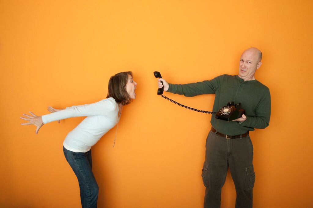 Woman yelling into rotary phone while man holds up ear and mouth piece of phone towards the woman's mouth. Topic: coaching agreement