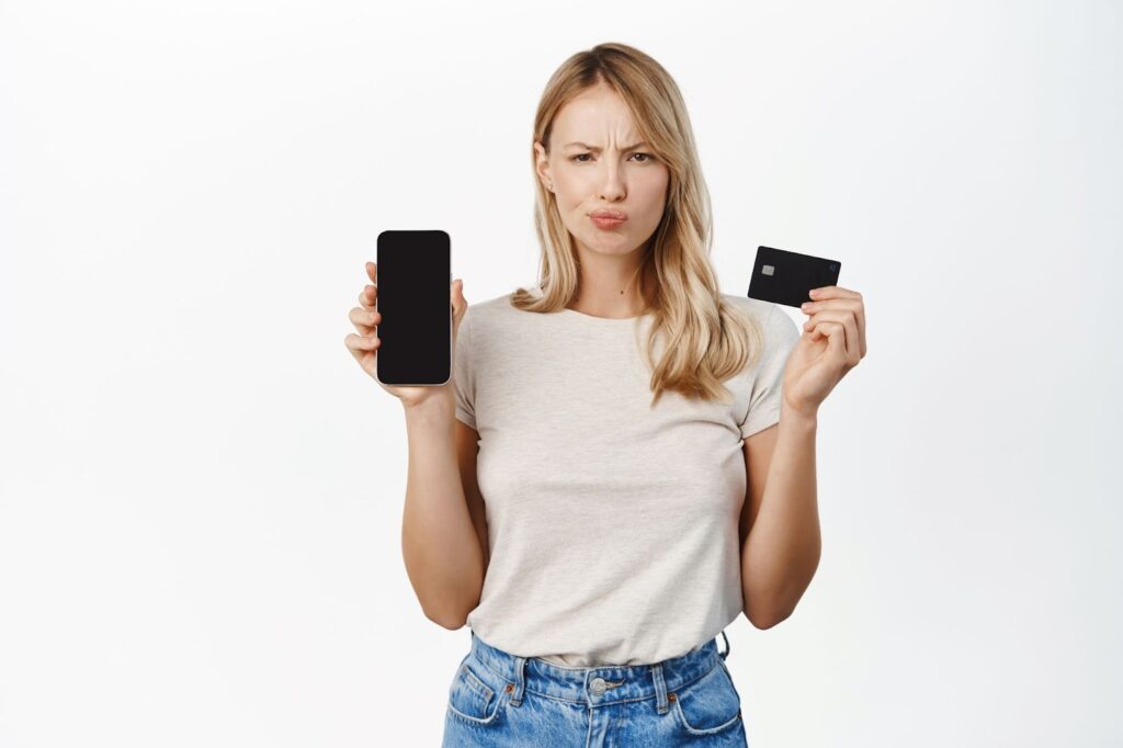 Woman holding up a cell phone on one hand and a credit card on the other hand with confused expression on her face. Topic: selling digital products