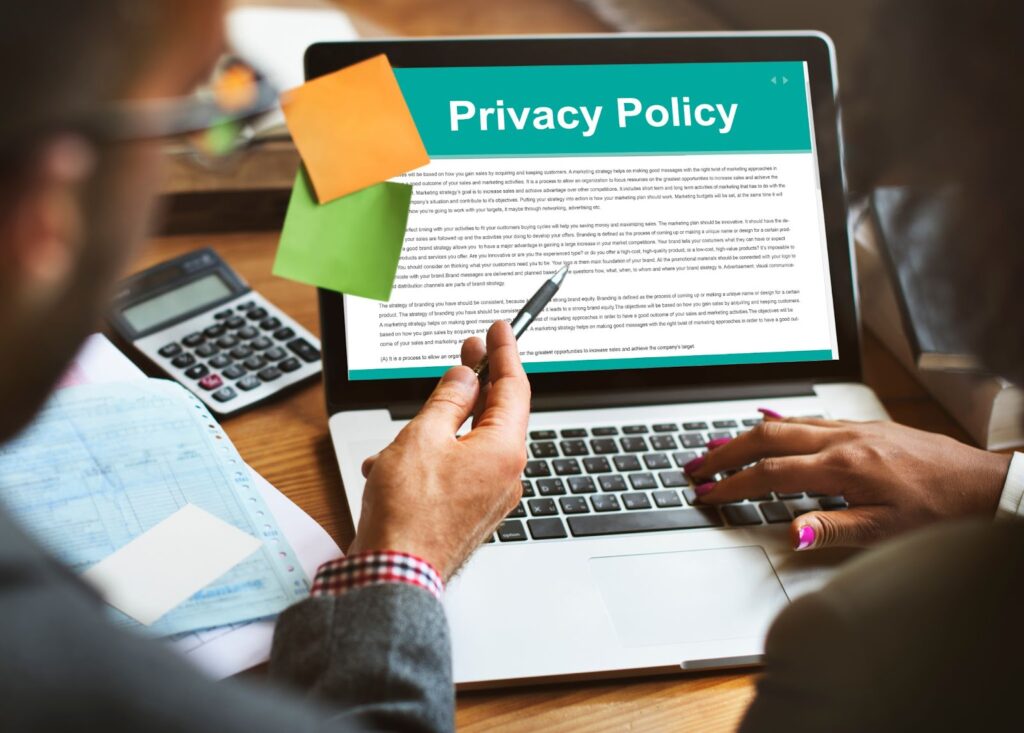 Blurred image of two people looking at the screen of a laptop. On the screen reads "Privacy Policy" while one person is pointing towards the screen with their pen. Topic: Data privacy in Online Business.