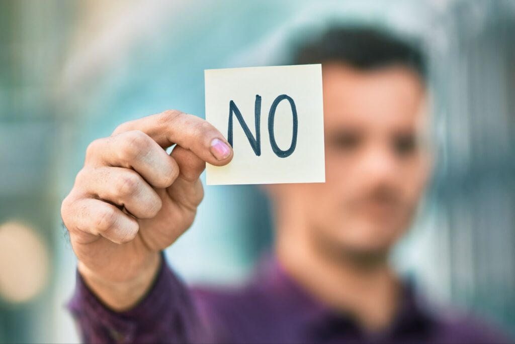 Man blurred in background while the foreground shows his hand holding out a post-it that reads "No". Topic: hiring digital freelancers