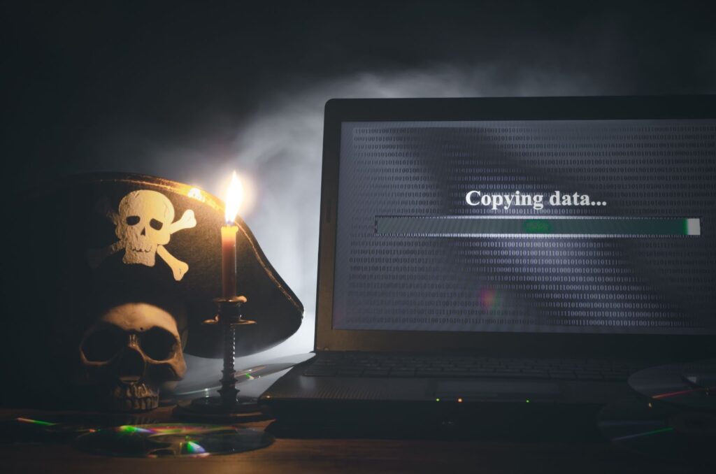 Dark background with image of darker computer screen, which reads "copying data..." on the screen. To the left of the computer is a skull with a pirate hat on and a single candle with a flame. Topic: protect online course content